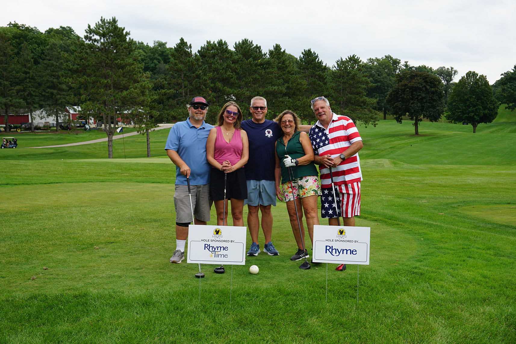 Four golfers stand next to Rhyme Time Scholarship signs at the Steve Ennis Memorial Golf Event